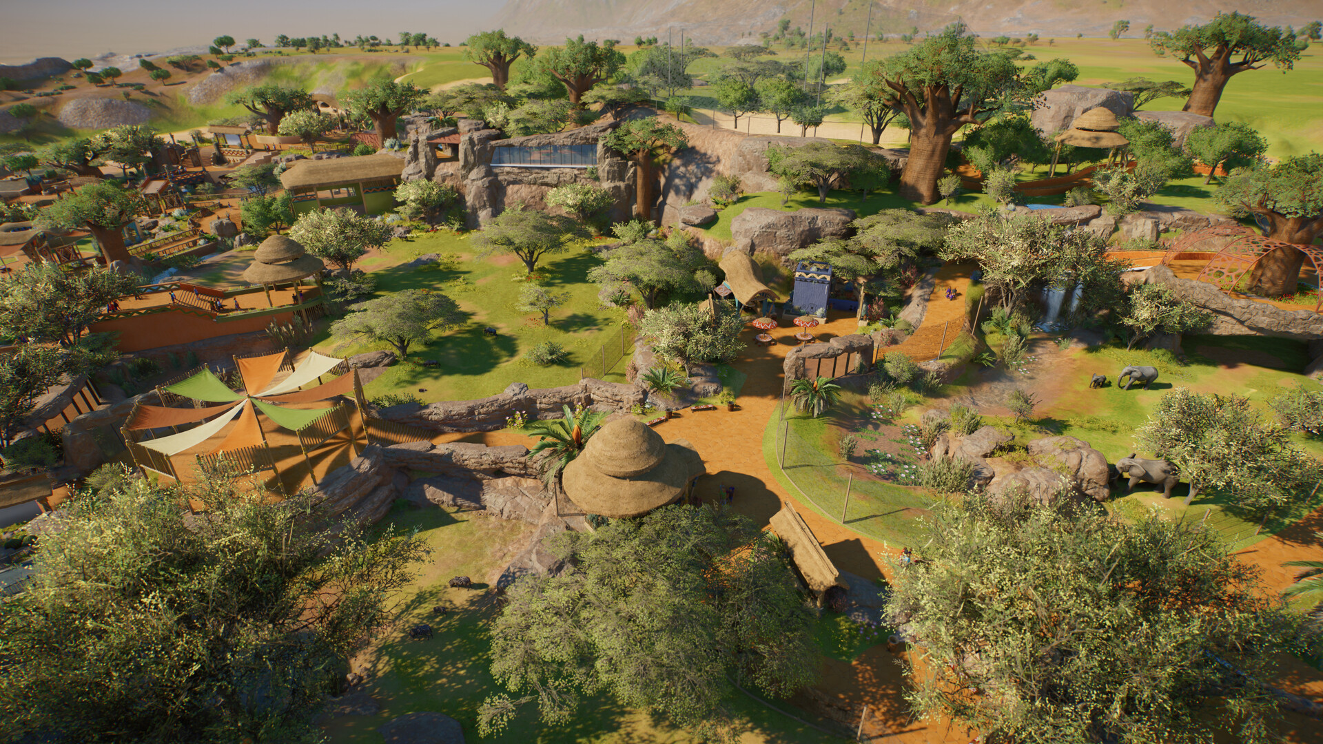 An aerial view of a savannah-themed zoo with baobab trees, thatched buildings, elephants and a glass viewing gallery cut into rock