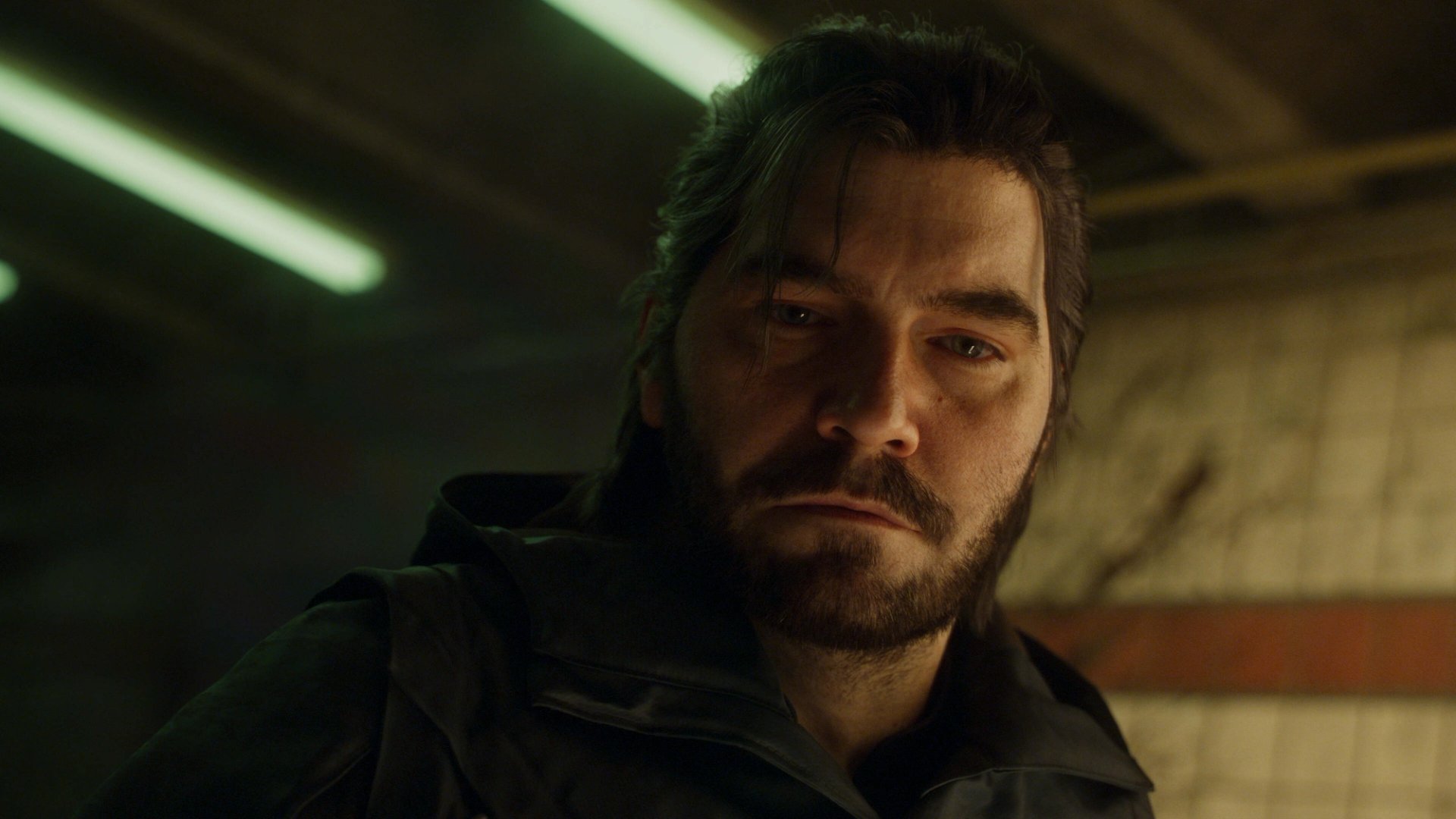 Close-up of Dylan Faden looking tired and wary under the harsh strip lights of a subway station