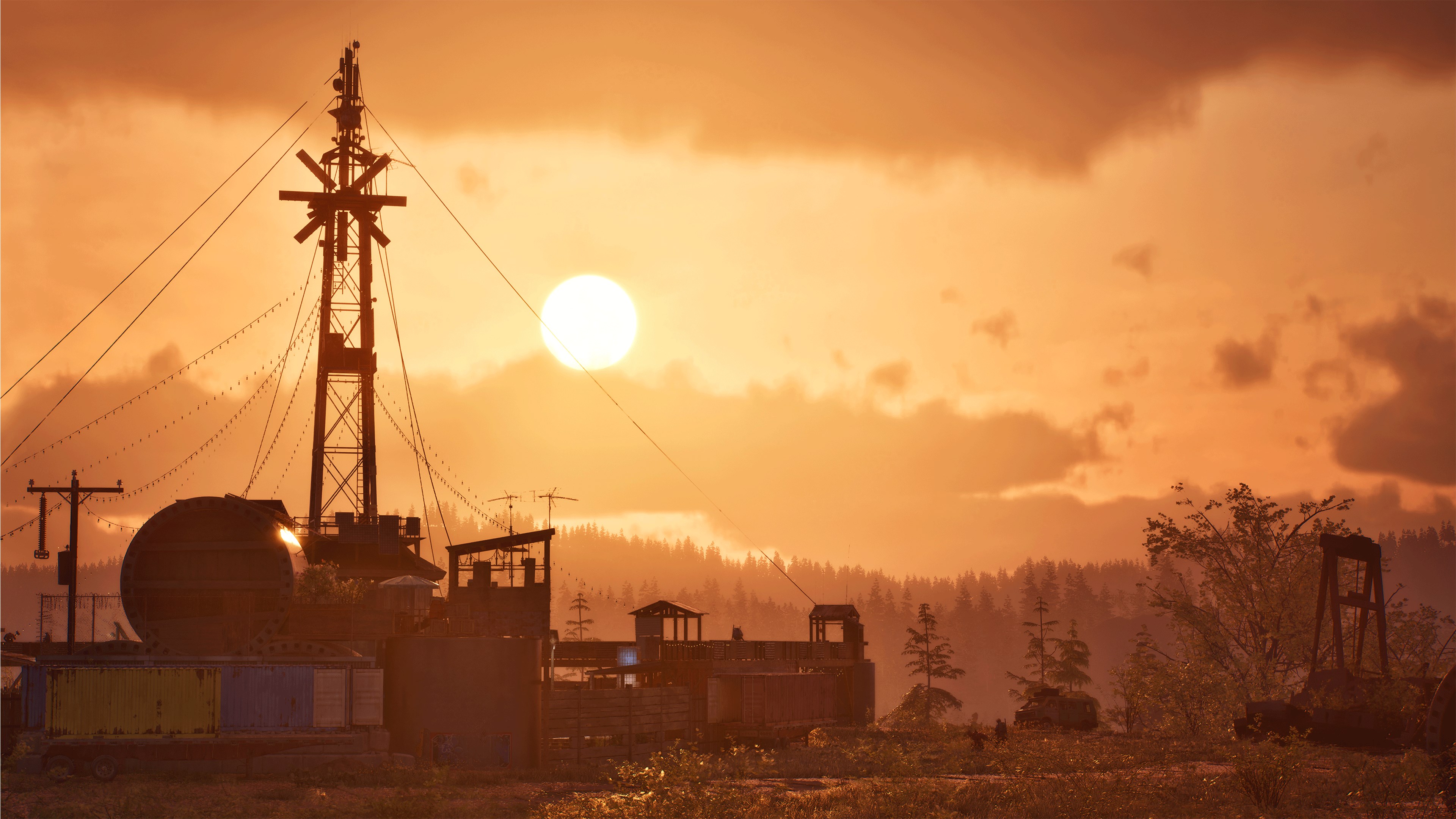 An industrial settlement silhouetted against an orange sunset, lattice towers and storage tanks standing over a fenced compound with forested hills behind