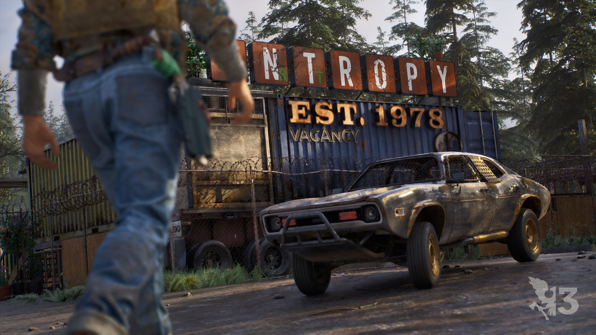A battered muscle car fitted with a welded push bar and mesh window screens sits outside a razor-wired compound as a survivor walks toward it.