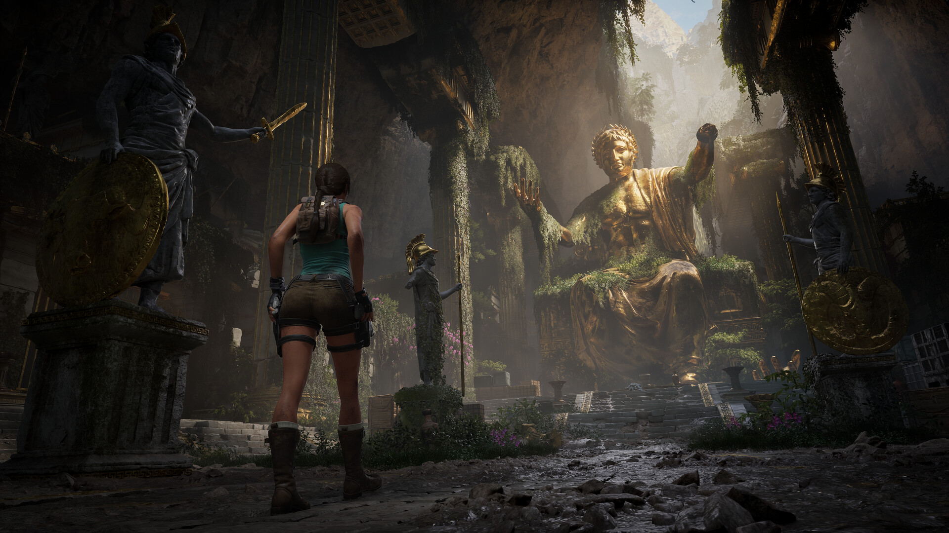 Lara Croft stands before a colossal gilded seated statue flanked by armoured warrior statues in the Greek ruins
