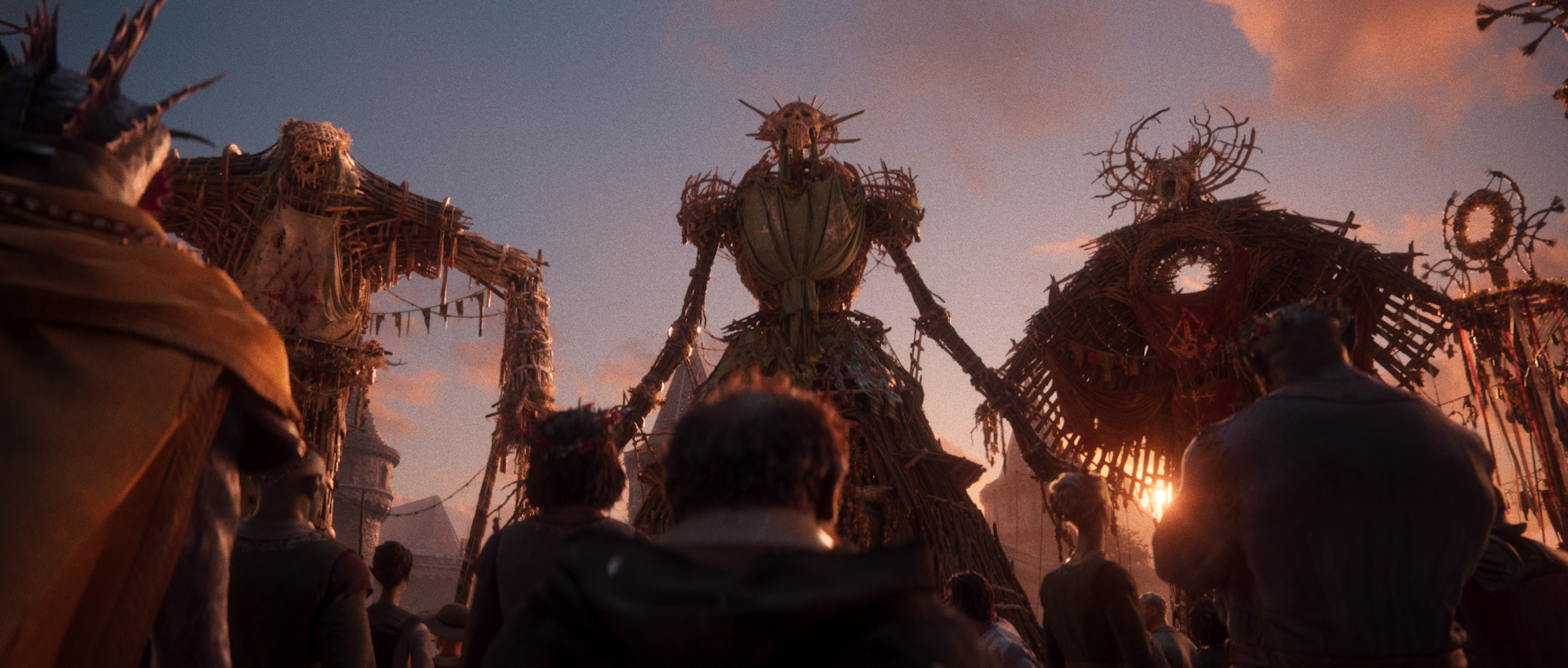 Trailer still of the crowd gathered beneath three towering wicker effigies at dusk