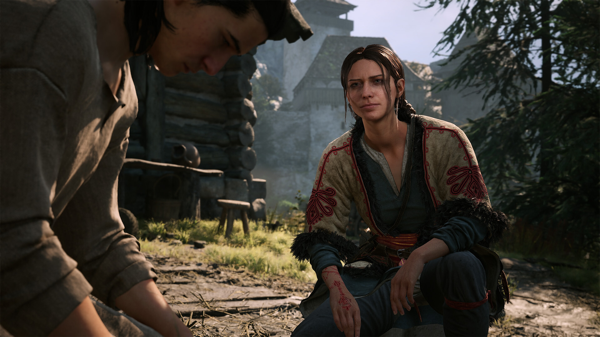 Two villagers sitting together in quiet conversation outside log houses, one in embroidered folk dress with a raw mark across her hand