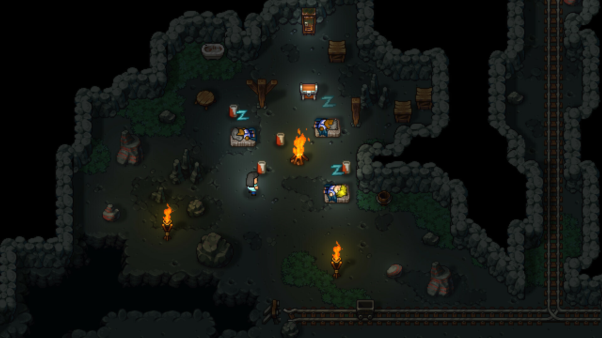 A dark cave interior in Streets of Rogue 2 lit by a campfire and two standing torches, with stone bunks holding sleeping NPCs, a treasure chest, striped barrels, crates and a mine cart on rails running along the wall