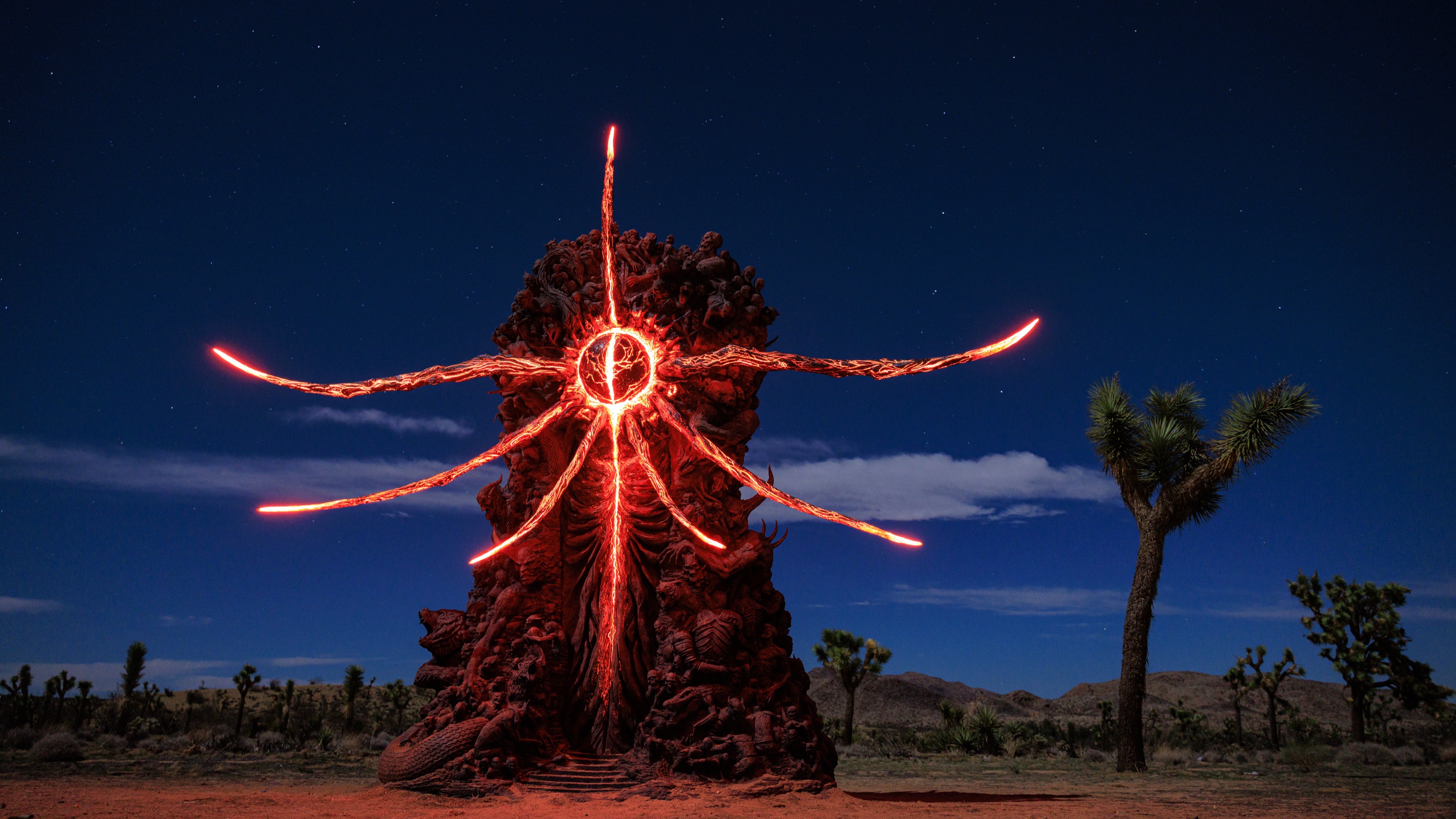 The Hellstone sculpture lit at night in the California desert at Joshua Tree, its red spokes glowing against the sky
