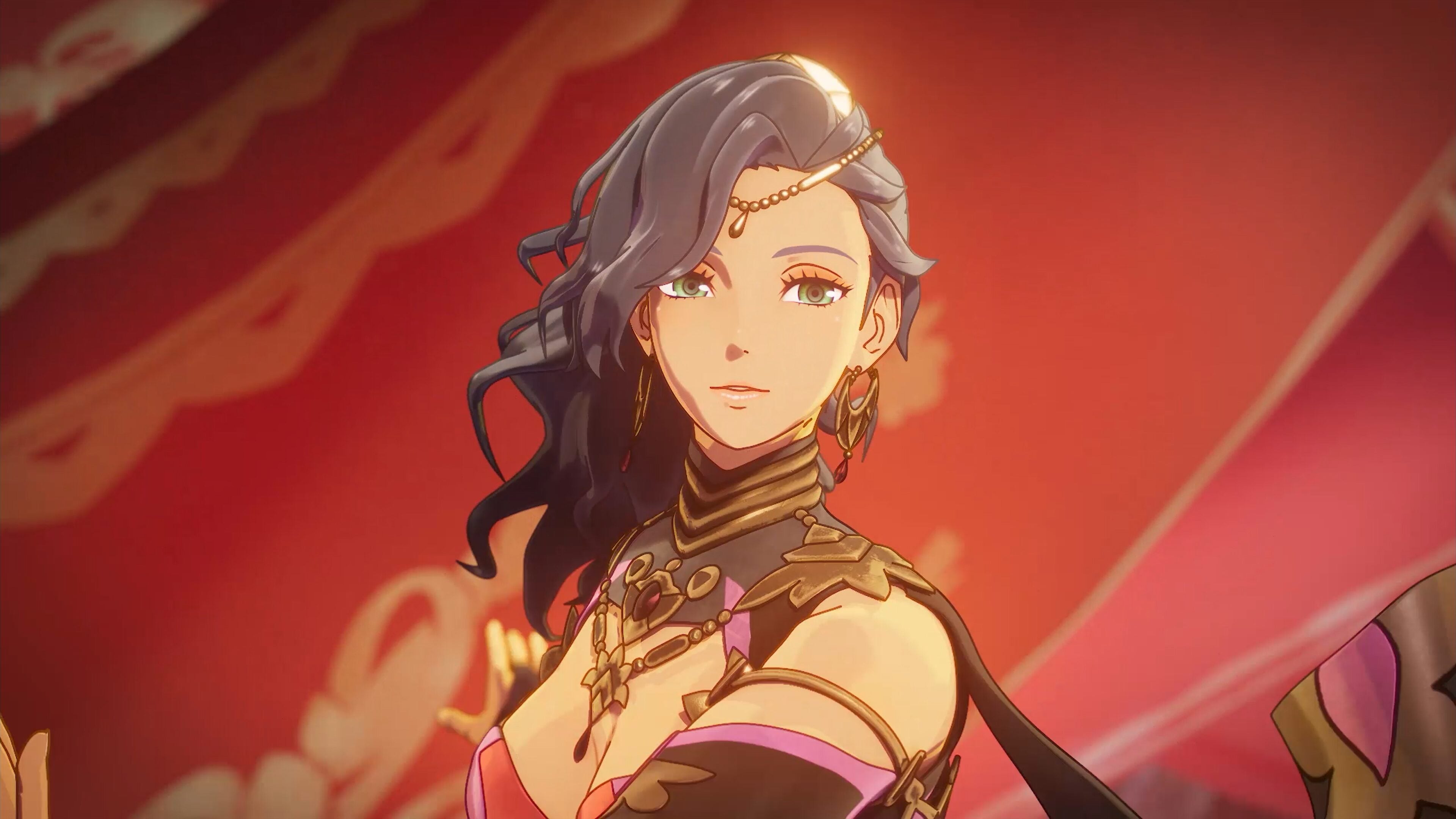 Close-up of Leda smiling against a red banner in her gold forehead chain and leaf earrings