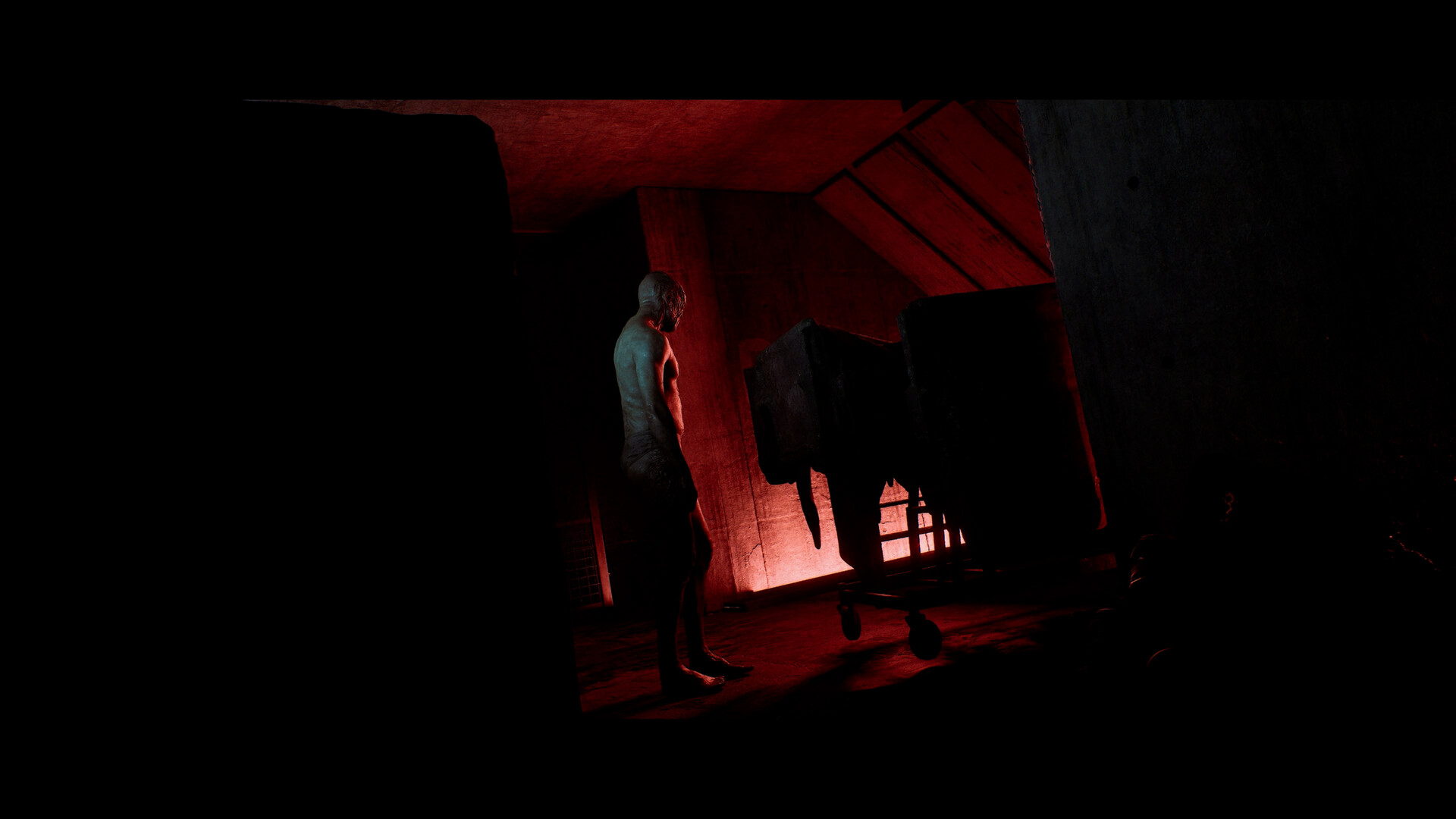 A pale humanoid figure standing in a red-lit room beside a trolley