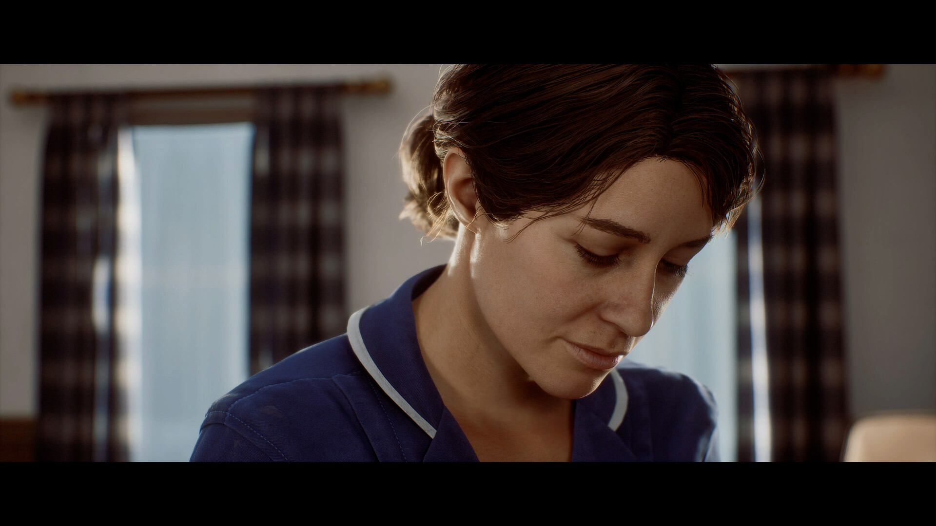 A woman in a care worker's uniform looks down in a curtained room